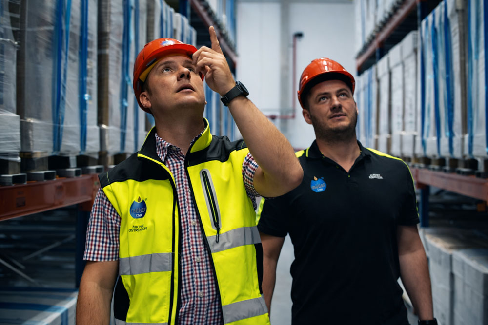 Workers wearing hard hats inspect a high-bay warehouse.
