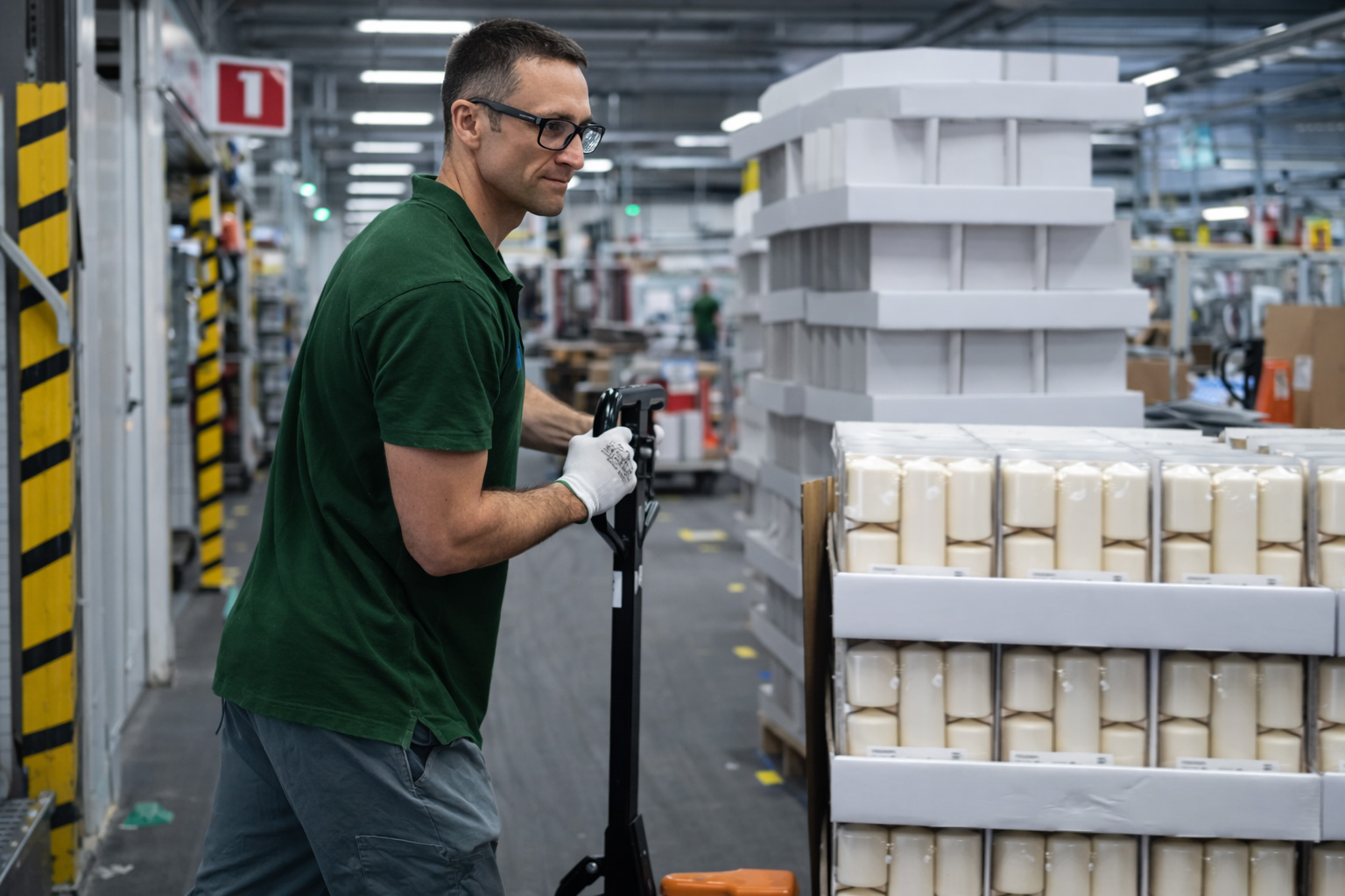 An employee moves a pallet of finished candle packs using a pallet truck.